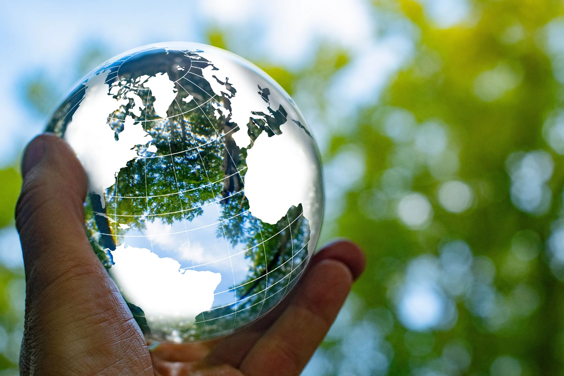 Focus on taking care of nature and the climate shown with a globe around a crystal ball with nature reflected inside and outside the ball. The ball is held by one hand.